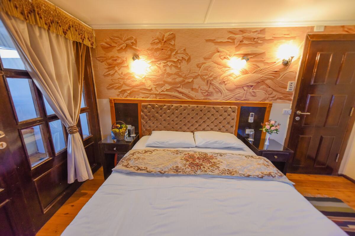 A bedroom with a large bed, a tufted headboard, floral wall decor, and two wall-mounted lights.