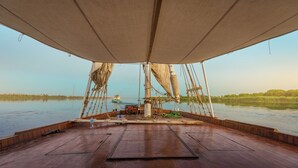 Cubierta de barco con un toldo grande, suelo de madera y vista al agua y follaje distante.