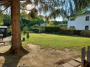 Ein Garten mit Rasen, einem Baum, einem Gartenhaus und einem Haus im Hintergrund.