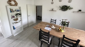 Et spiseområde med et træbord, stole, en hvid reol og en hængende lampe.