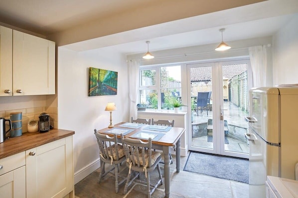 A kitchen with a dining table, chairs, a coffee machine, and a refrigerator.