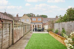 A backyard with a lawn, a wooden fence, and a house with a tiled roof.