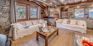 Relax in this cozy cabin living area, featuring plush sofas and a wooden coffee table, surrounded by stunning views of the snowy landscape.