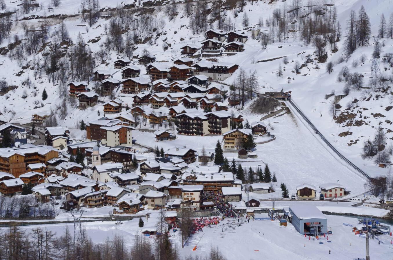 A snow-covered village with wooden buildings, a ski slope, and a small building with a blue roof.