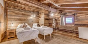 Cozy bedroom with two single beds, bedside tables, and lamps, set amidst a rustic wooden ceiling with exposed beams.