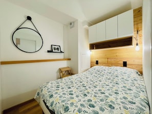 A bedroom with a bed, a wooden headboard, a wall-mounted mirror, and a small wooden stool.
