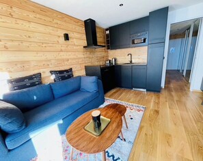 A modern living space with a sofa, coffee table, and a kitchen area with cabinets and appliances.