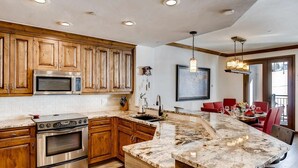 A kitchen with wooden cabinets, a built-in microwave, a stove, and a marble island. - Highlands Slopeside #207 3 Bedroom Condo by RedAwning (Avon)