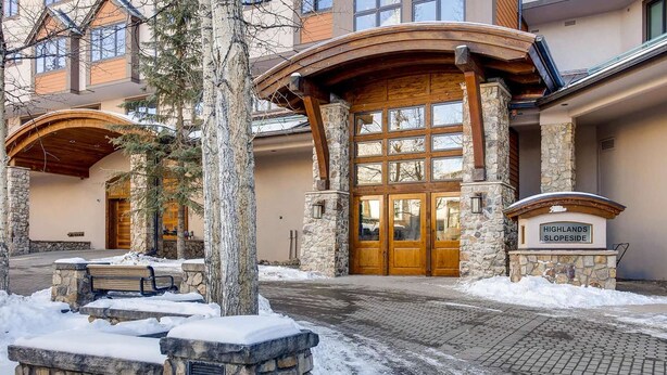 A building entrance with a stone facade, wooden doors, and a sign reading "Highlands Slopeside". - Highlands Slopeside #207 3 Bedroom Condo by RedAwning (Avon)