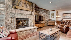 A cozy living room with a stone fireplace, leather furniture, and artwork on the walls. - Highlands Slopeside #207 3 Bedroom Condo by RedAwning (Avon)
