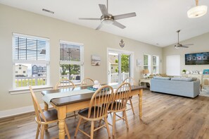 Un salon spacieux comprenant un coin repas, de grandes fenêtres et un ventilateur de plafond.