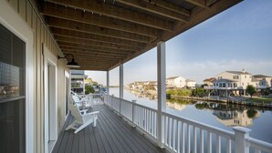 A covered wooden deck with white railings overlooking a calm water body and residential buildings.