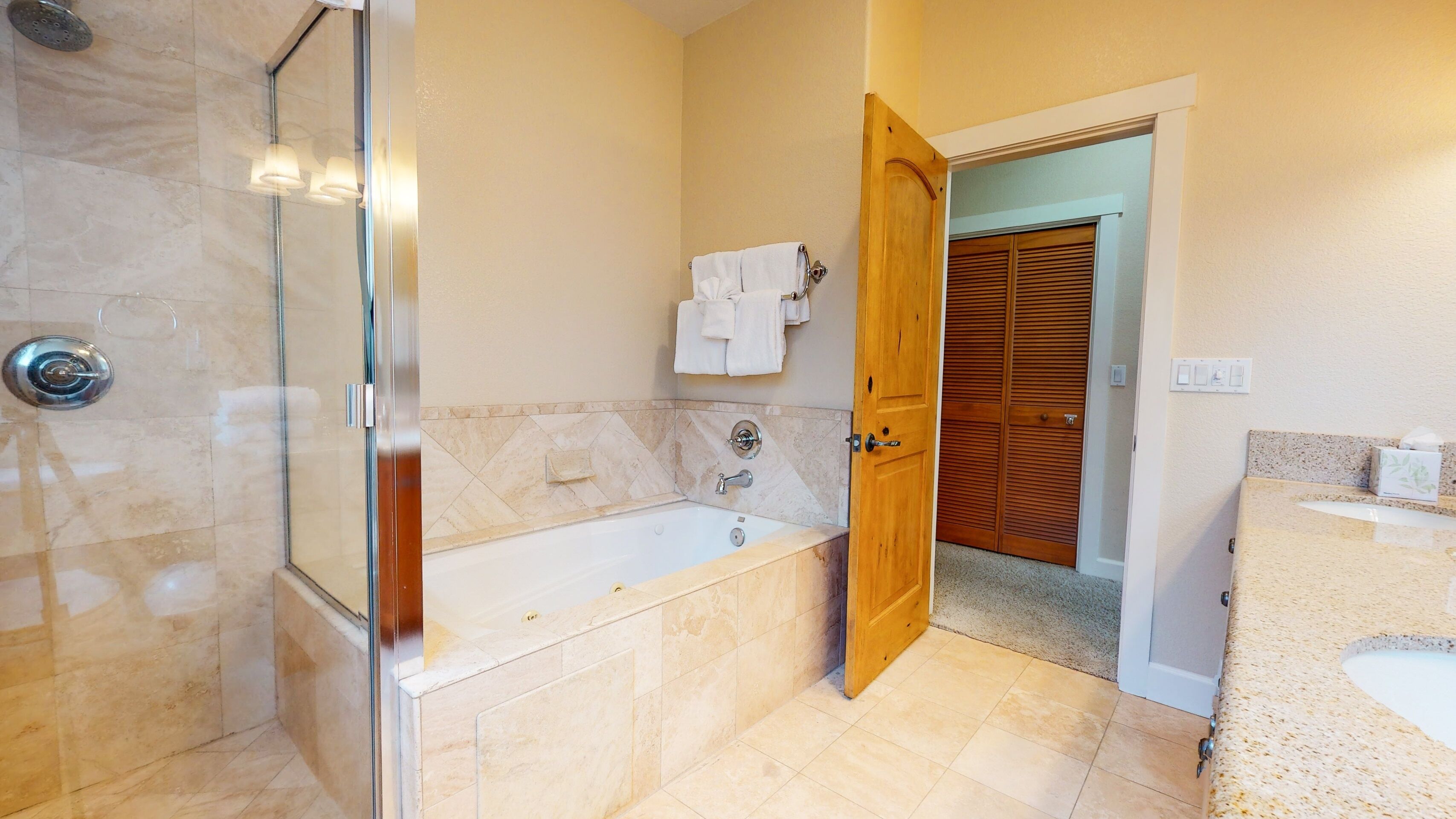 A bathroom with a glass-enclosed shower, a bathtub, and a wooden door leading to a closet.