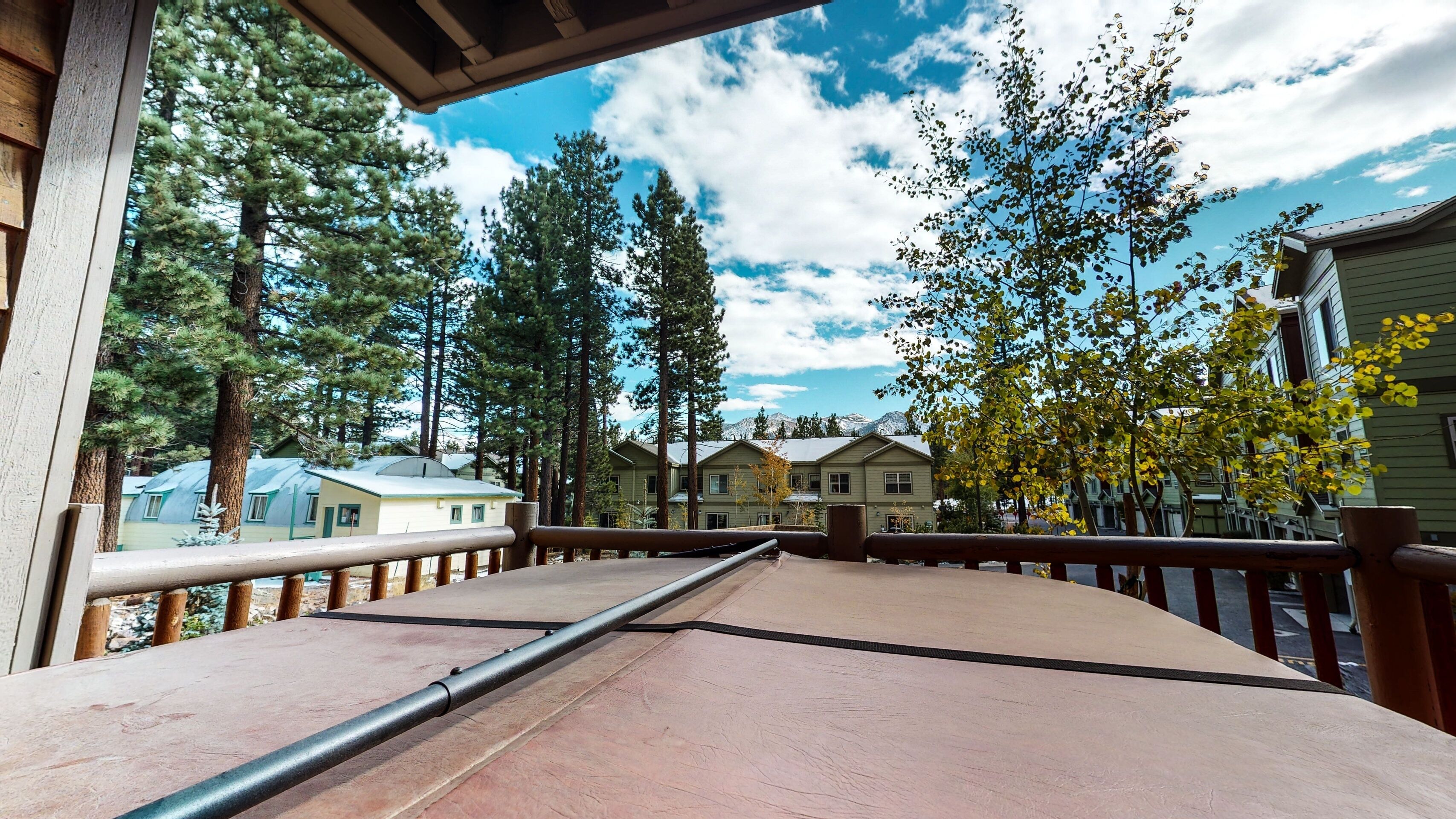 A wooden deck with a metal railing overlooking a row of houses and tall trees.