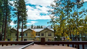 A view of a building with multiple windows and a balcony, surrounded by trees and mountains in the background. - Mammoth Gateway Village 7 Pet-Friendly, Mountain Modern with Private Jacuzzi and 2 Car Garage by RedAwning (Mammoth Lakes)