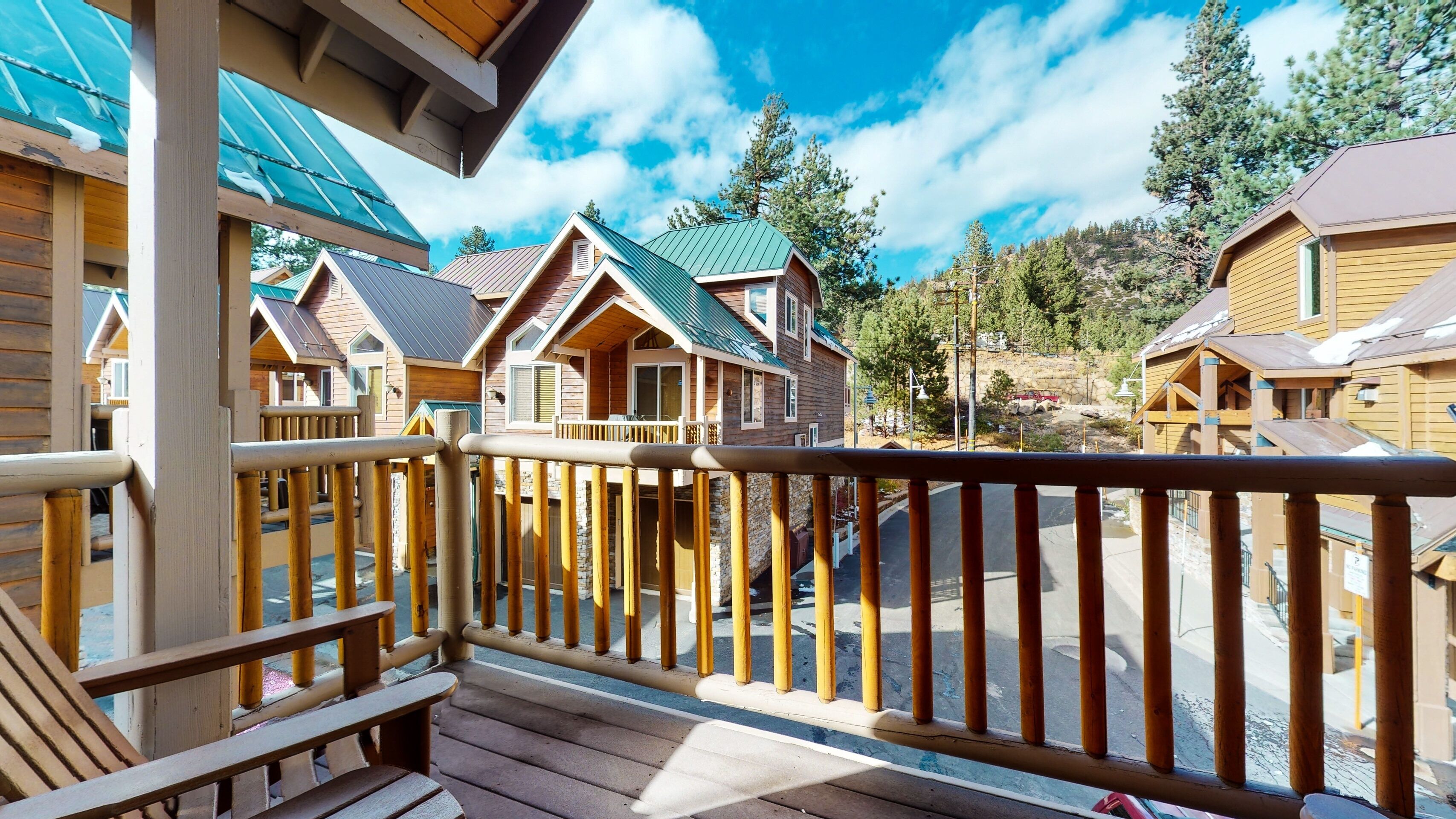 A wooden deck with a railing overlooking a row of cabins with green roofs.
