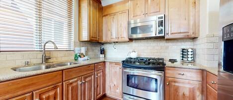 A kitchen with wooden cabinets, a stainless steel stove, a microwave, and a sink.