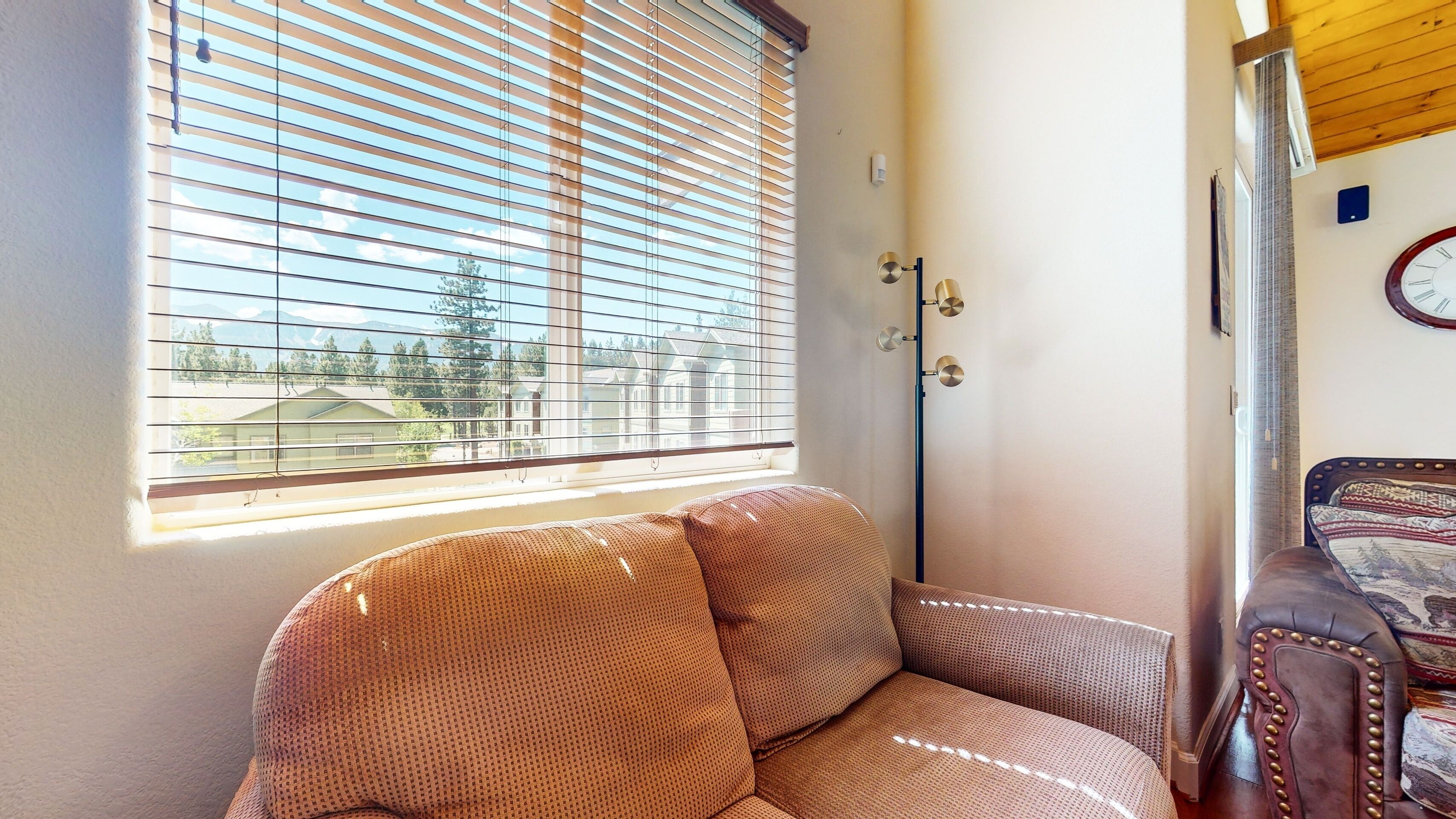 A room with a large window, a sofa, a lamp, and a clock on the wall.