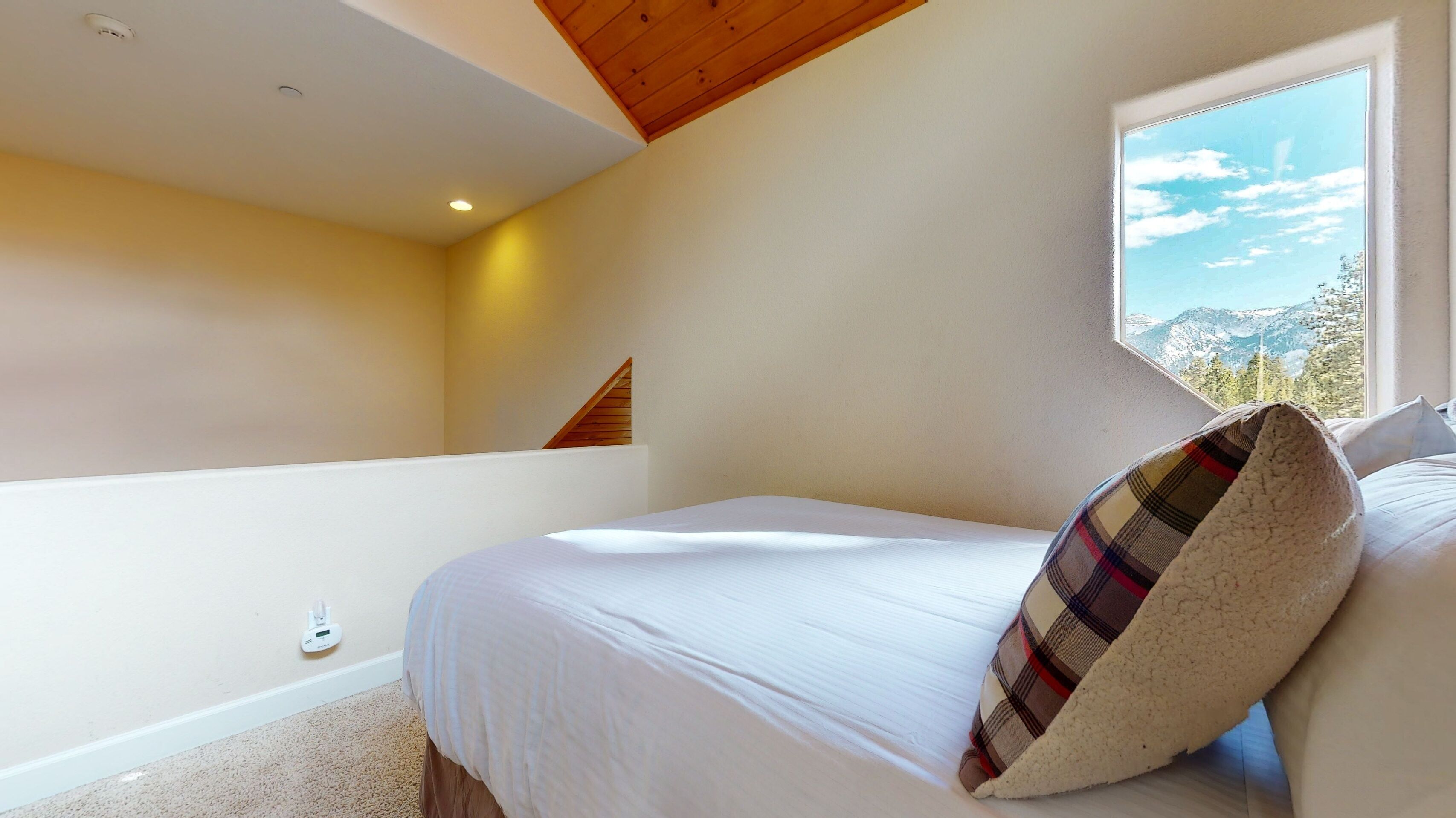 Un dormitorio con cama, ventana con vistas a la montaña, techo de madera y pared blanca.