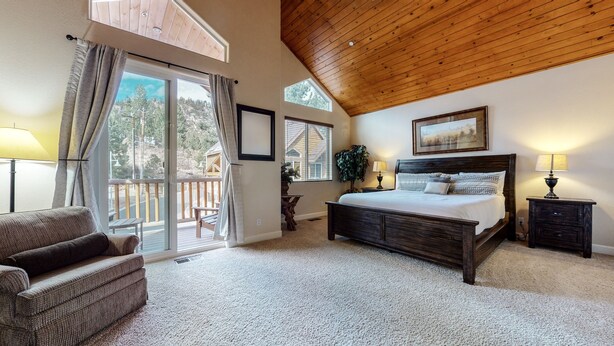 A bedroom with a large bed, a wooden ceiling, and a balcony with a view of trees. - Mammoth Gateway Village 7 Pet-Friendly, Mountain Modern with Private Jacuzzi and 2 Car Garage by RedAwning (Mammoth Lakes)