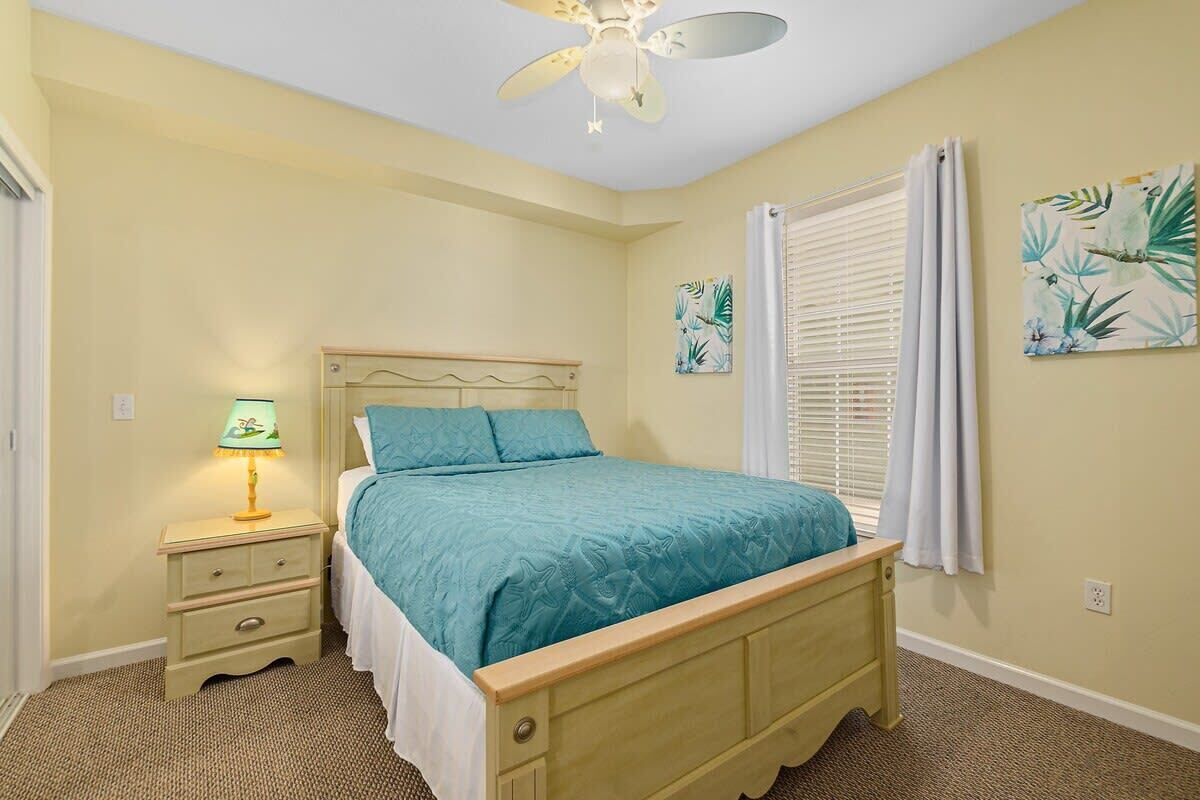 A bedroom with a bed, a nightstand, a ceiling fan, and two wall-mounted paintings.