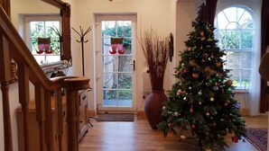 Un ampio soggiorno con una scala in legno, un grande albero di Natale e uno specchio decorativo.