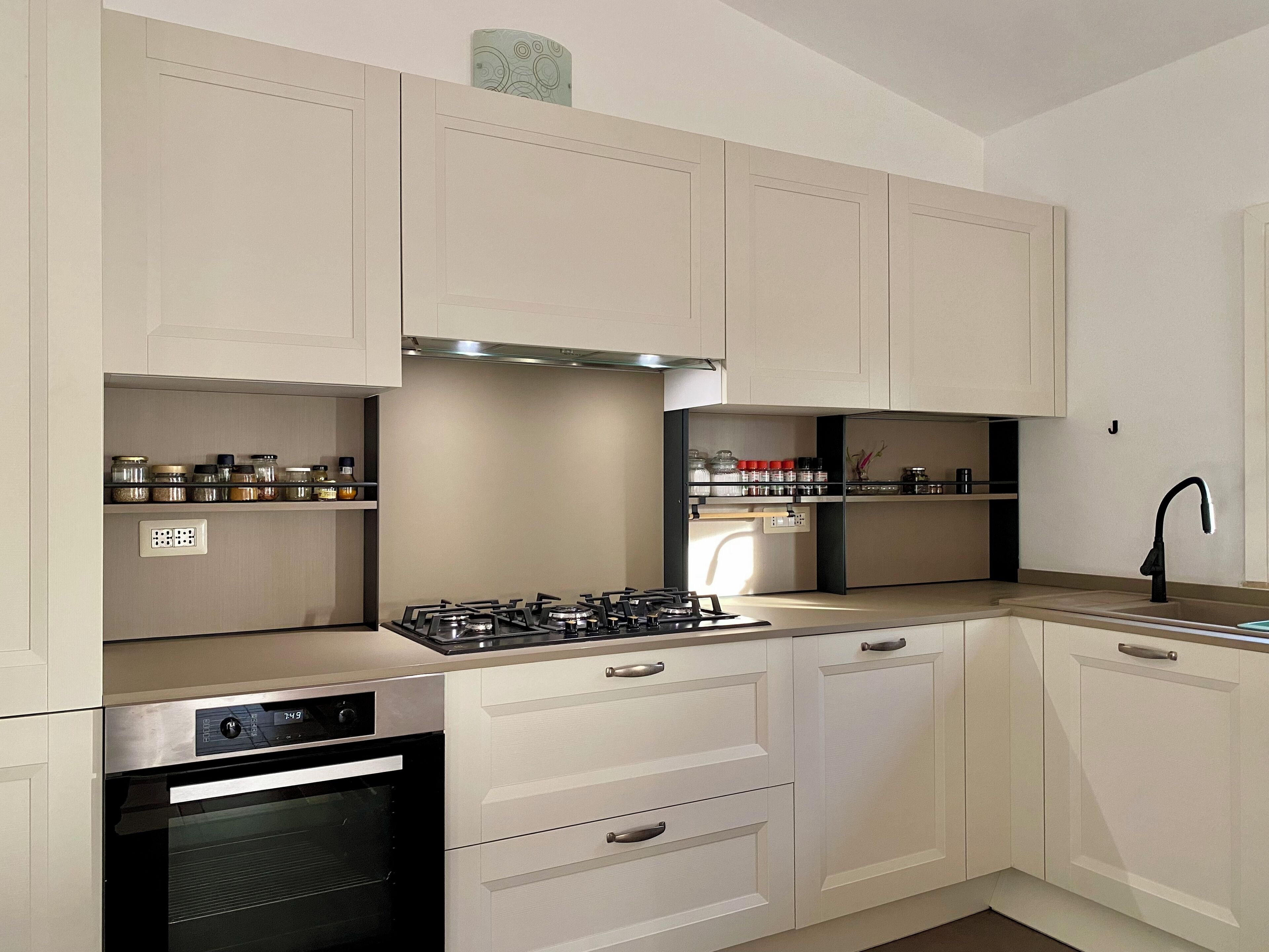 A modern kitchen with white cabinetry, a gas stove, an oven, and a sink with a black faucet.