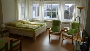 Et soveværelse med seng, to stole, et skrivebord og en lampe.