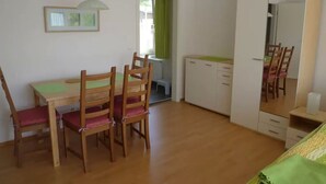 Et værelse med et træbord, stole, et tekøkken, en garderobe og et spejl.