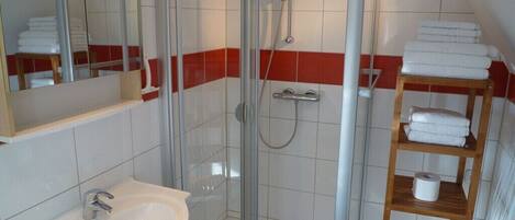 A bathroom with a glass-enclosed shower, a sink, and a wooden shelf with towels.