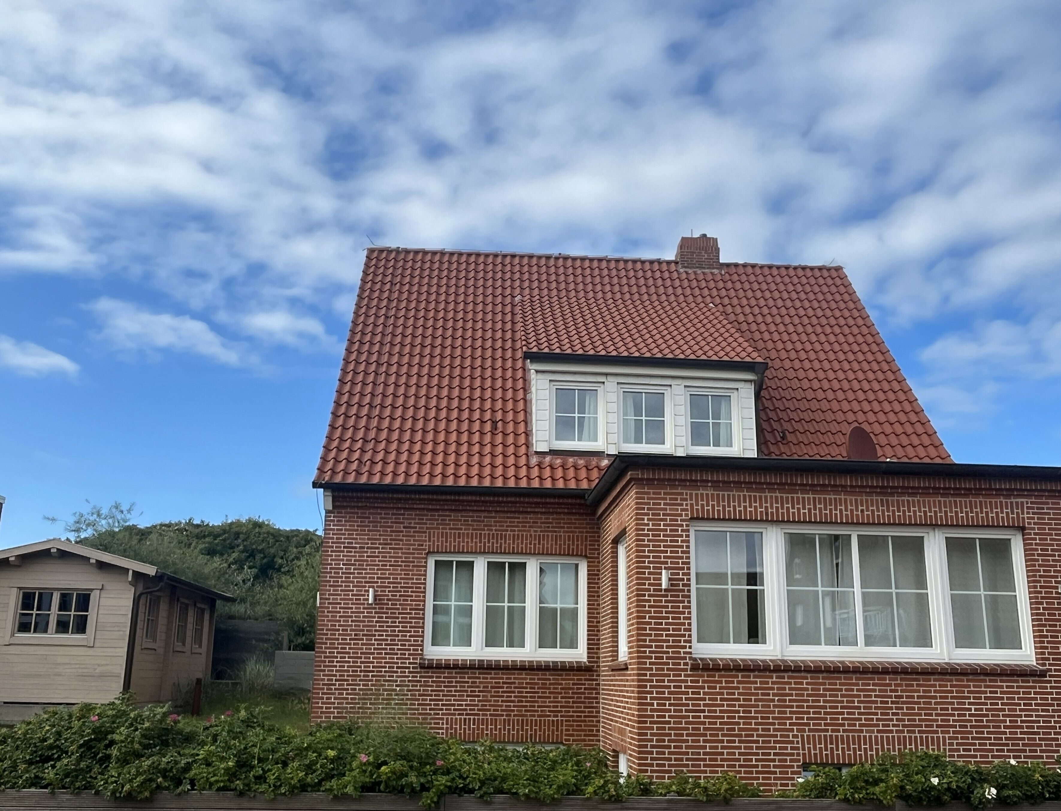 Ein zweistöckiges Backsteinhhaus mit rotem Ziegeldach und weißen Fensterrahmen.
