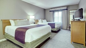 Ein Hotelzimmer mit zwei Betten, einem Schreibtisch, einem Fernseher und einem Fenster mit Vorhängen.