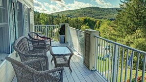 Eine Holzterrasse mit Korbmöbeln und einem Glastisch, mit Blick auf ein bewaldetes Tal.