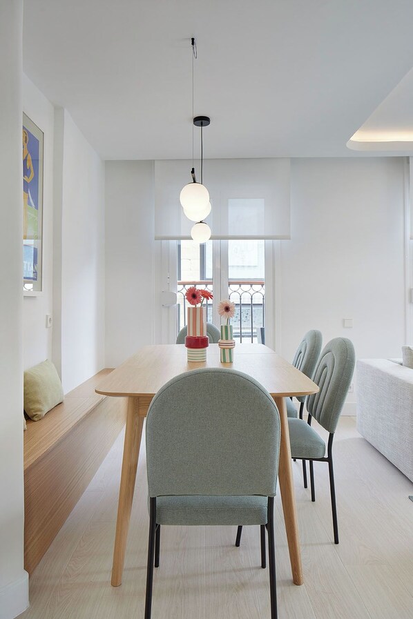 A modern dining area with a wooden table, grey upholstered chairs, and a hanging light fixture. - San Juan by FeelFree Rentals (San Sebastián)