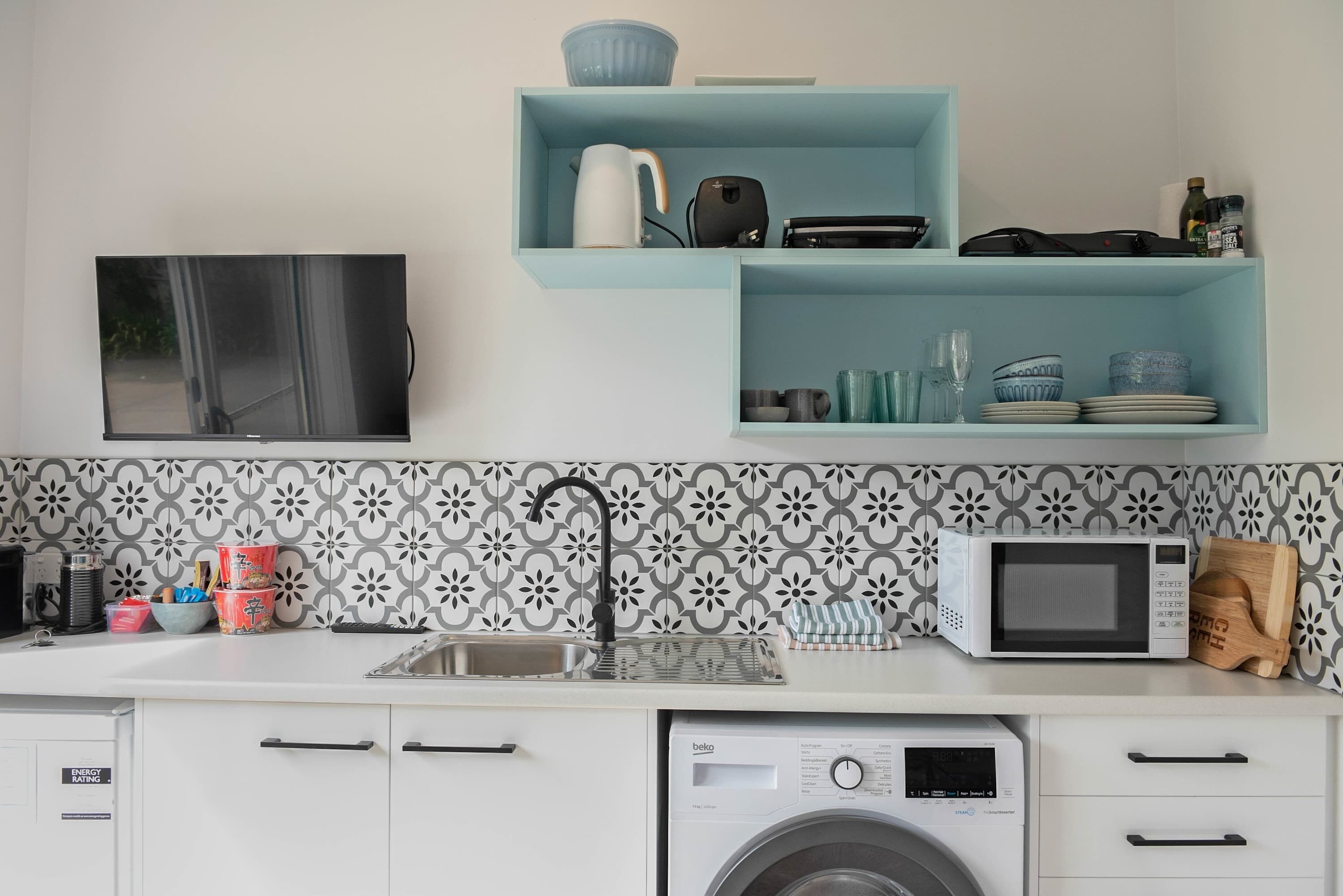 A kitchen with a washing machine, microwave, sink, and a flat-screen TV.