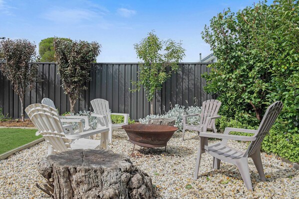A patio with Adirondack chairs, a fire pit, and a wooden stump.