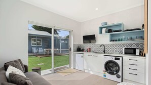 A modern kitchen with a washing machine, a microwave, and a TV on the wall. - Wild Rose Studio, 100M to the water (Goolwa South)