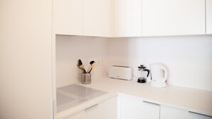 Et moderne køkken med hvide skabe, en brødrister, kaffemaskine og elkedel.