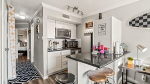 A modern kitchen with white cabinets, a microwave, a sink, and a bar area with stools. - Beach Condo by 61st Fishing St Pier • Clean, Loved & Steps to Beach, heated pool (Galveston)