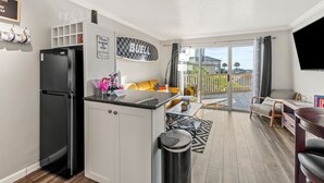 A compact kitchen with a black refrigerator, a small dining area with a table and chairs, a sofa, and a large window overlooking a balcony. - Beach Condo by 61st Fishing St Pier • Clean, Loved & Steps to Beach, heated pool (Galveston)