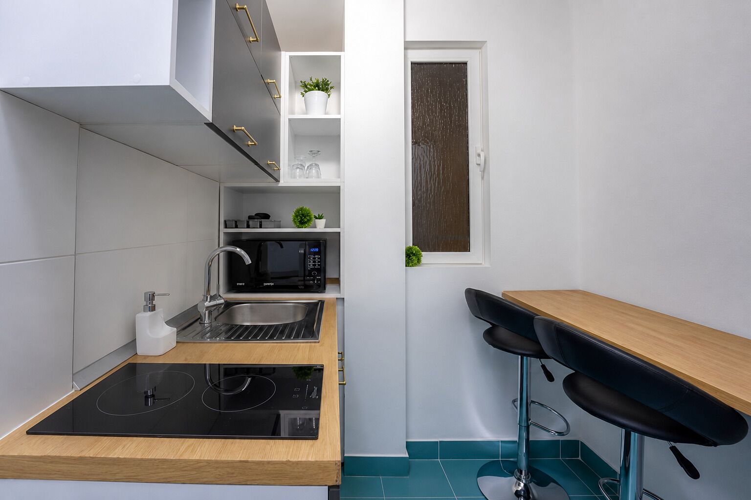 Una cocina compacta con microondas integrado, un lavamanos y una pequeña encimera.