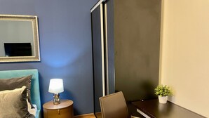 A compact room with a bed, a desk, a chair, a lamp, and a small plant. - Metropole Apartments Studio City (Bucharest)