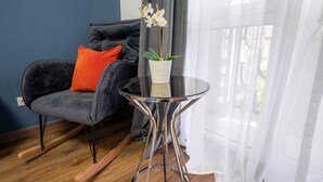 A modern living room with a dark grey sofa, a white vase with an orchid, and a glass table with a metal base. - Metropole Apartments Studio City (Bucharest)