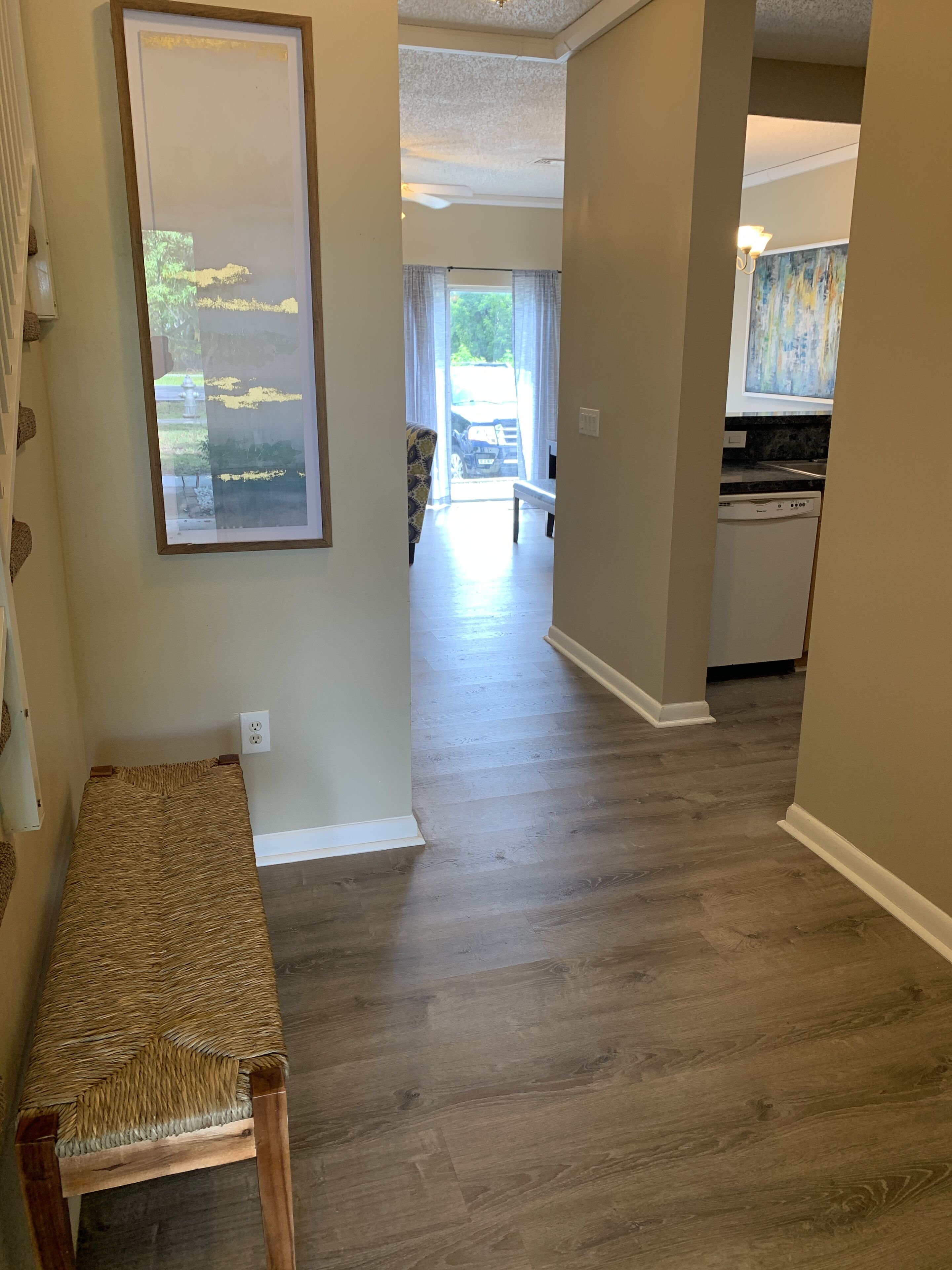 A hallway with a woven bench, a dining area with a table and chairs, and a kitchen with a dishwasher.