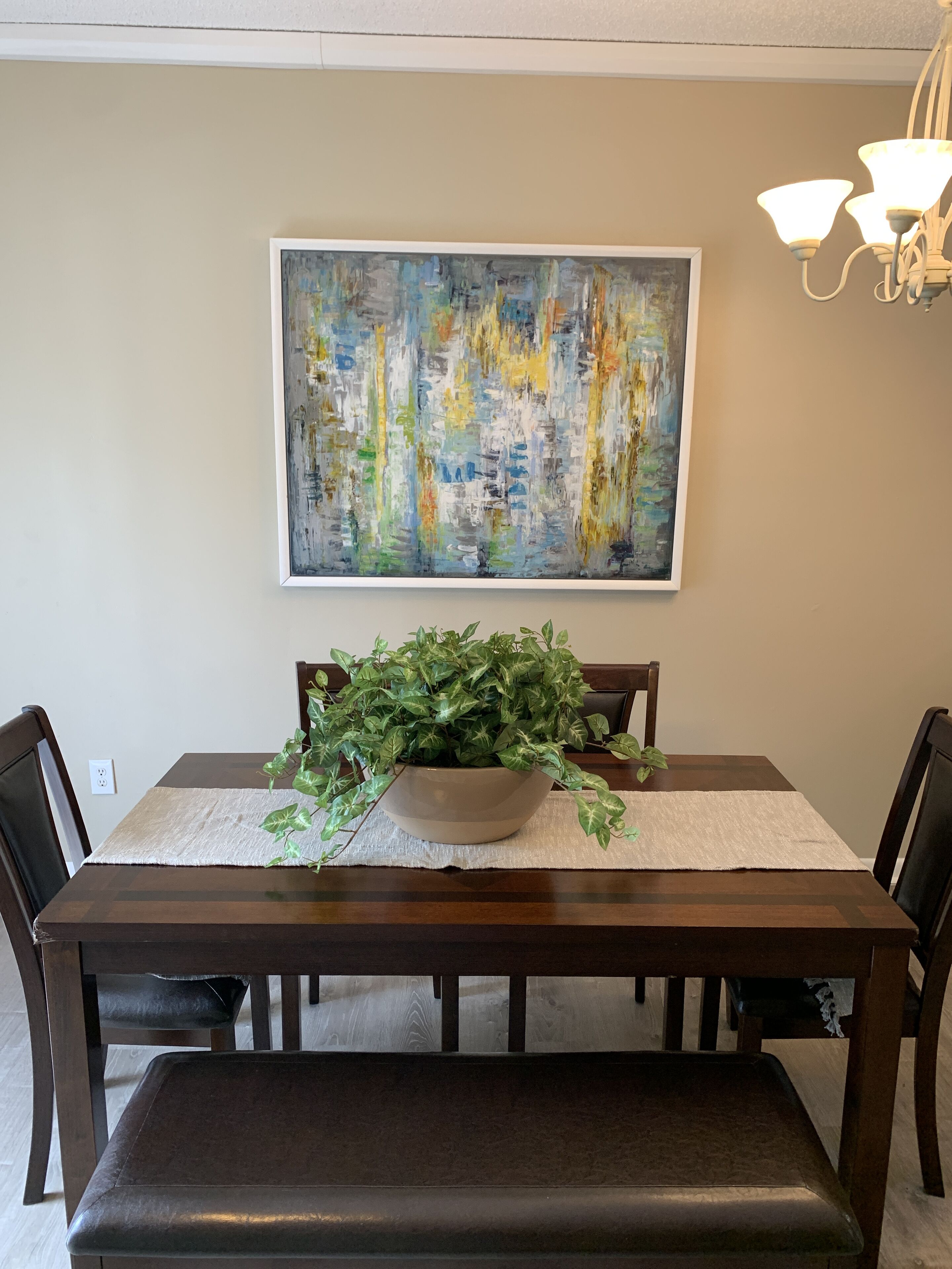 Een eettafel met daarboven een groot abstract schilderij, omringd door donkerhouten stoelen.