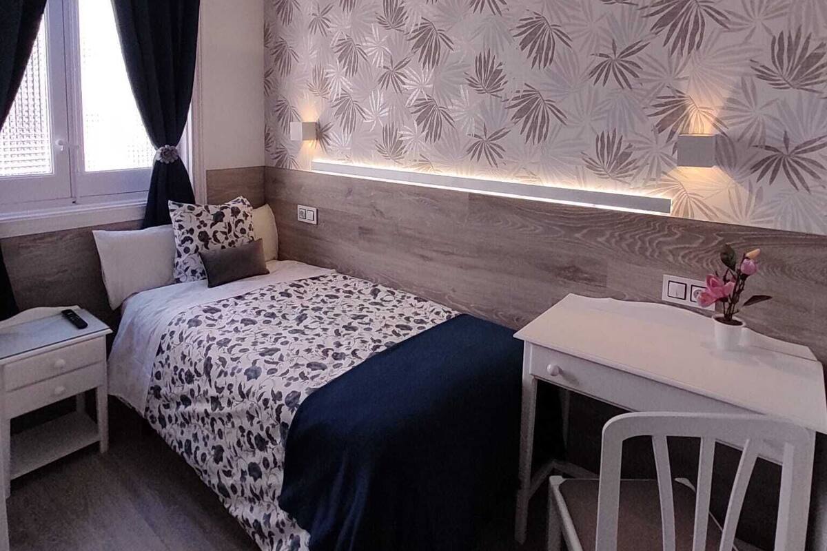 A modern bedroom with a bed, bedside table, and a desk with a chair.