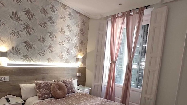 Ein Schlafzimmer mit einem großen Bett, einem Nachttisch, einer Lampe und einem Fenster mit Vorhängen.