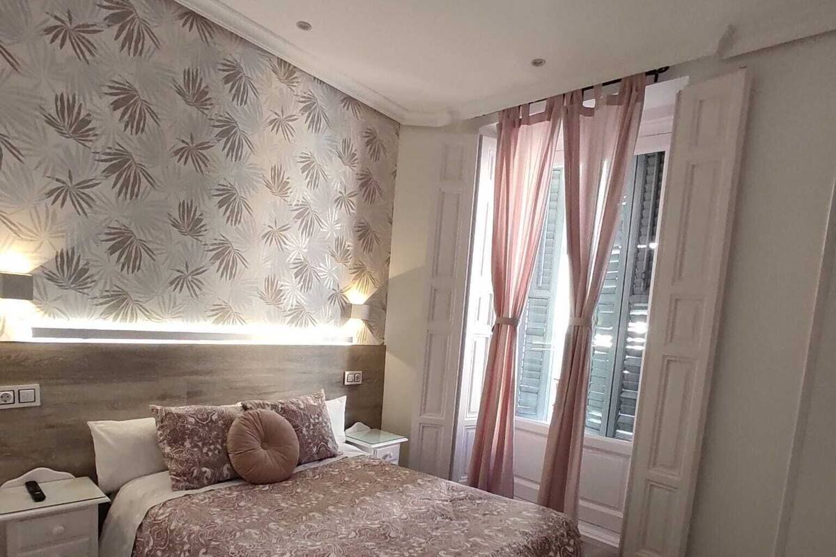 A bedroom with a large bed, a bedside table, a nightstand, a lamp, and a window with curtains.