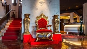 A grand lobby with a red carpeted staircase, a luxurious red velvet chair, and ornate golden columns. - Cesare Augustus (Jesolo)