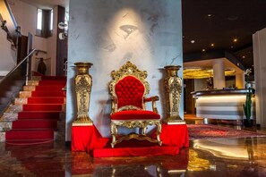 A grand lobby with a red carpeted staircase, a luxurious red velvet chair, and ornate golden columns. - Cesare Augustus (Jesolo)
